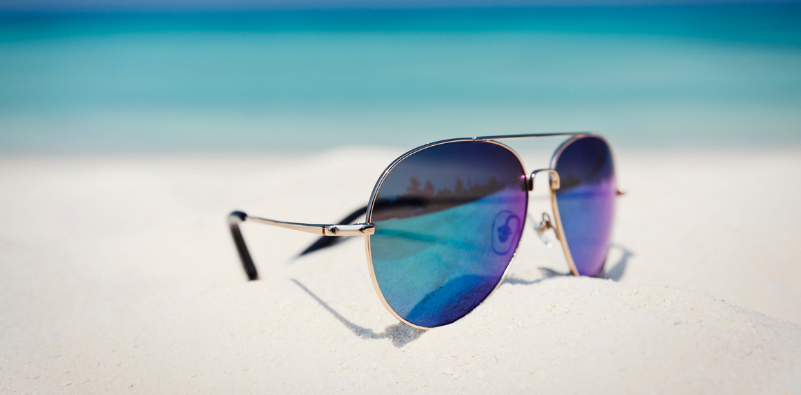 – A pair of aviator-style sunglasses on white sand