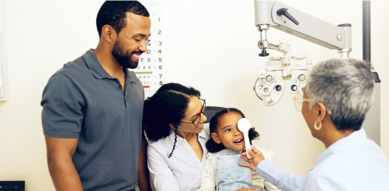 A family in the testing room at the opticians, while the optometrist tests the daughter's vision.