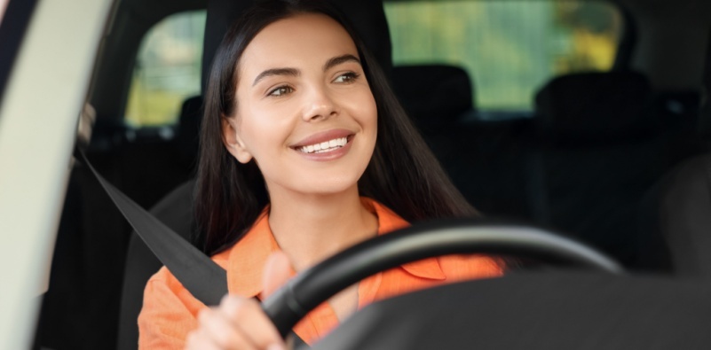 A young woman driving in her car, smiling