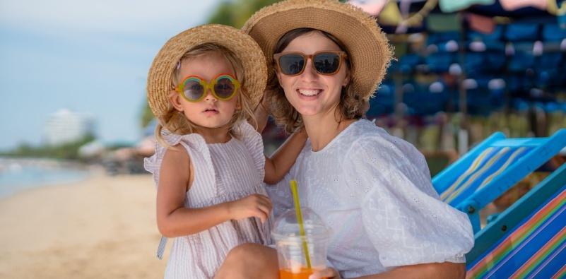 A young girl and her mum on the beach, both wearing a wide-brimmed hat and sunglasses